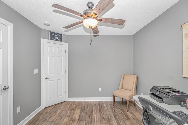 living area with ceiling fan, a textured ceiling, baseboards, and wood finished floors