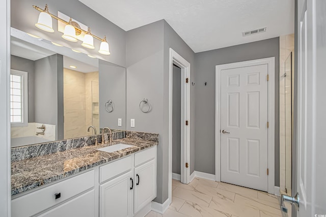 full bath featuring baseboards, visible vents, marble finish floor, a tile shower, and vanity