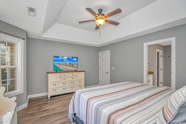 bedroom with ceiling fan, wood finished floors, visible vents, baseboards, and a raised ceiling