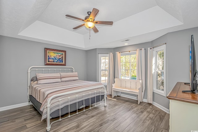 bedroom with baseboards, a tray ceiling, and wood finished floors