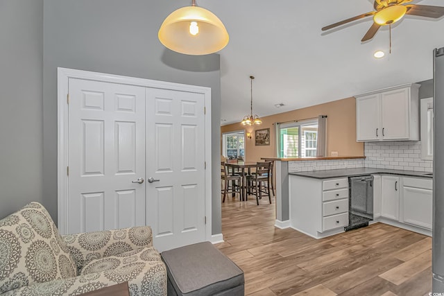 kitchen with dark countertops, decorative backsplash, white cabinets, light wood-type flooring, and a peninsula