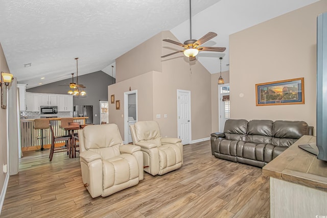 living room featuring a textured ceiling, high vaulted ceiling, light wood-type flooring, and a ceiling fan