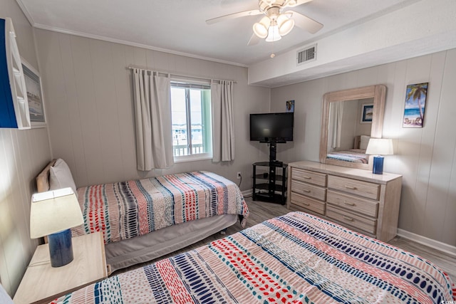 bedroom with baseboards, visible vents, a ceiling fan, ornamental molding, and wood finished floors