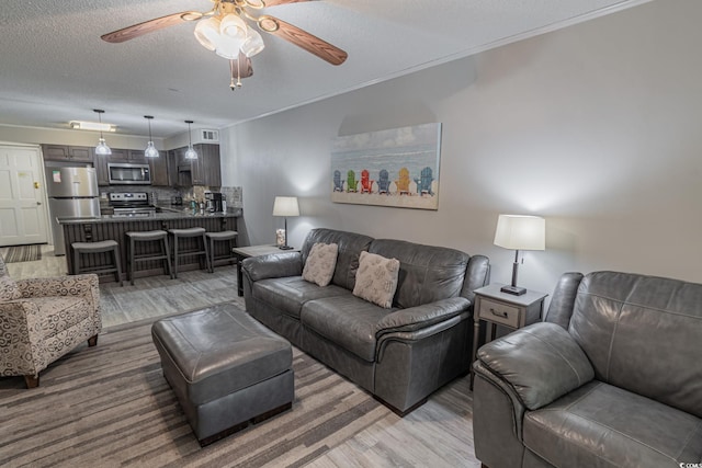 living area with ceiling fan, ornamental molding, a textured ceiling, and light wood-type flooring