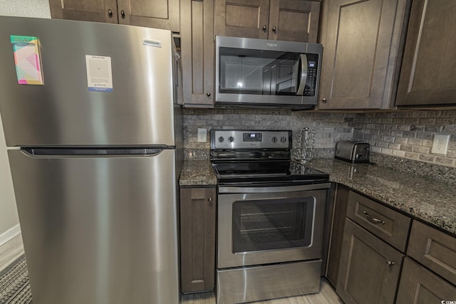 kitchen featuring dark brown cabinets, tasteful backsplash, stainless steel appliances, and dark stone countertops