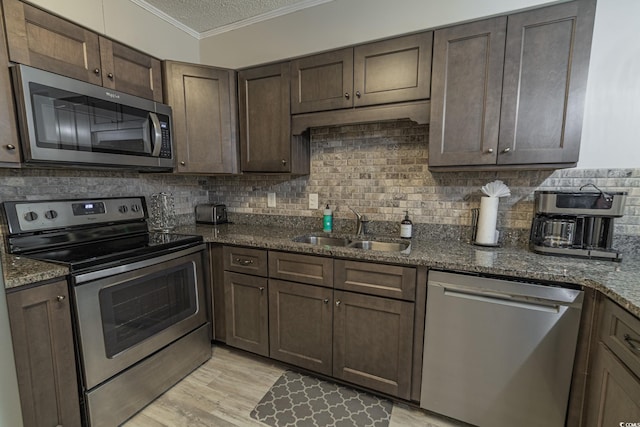 kitchen featuring stainless steel appliances, decorative backsplash, ornamental molding, a sink, and dark brown cabinets