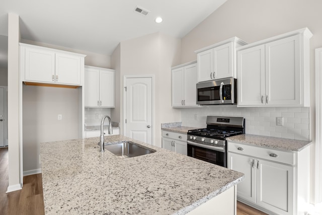 kitchen featuring a kitchen island with sink, stainless steel appliances, a sink, white cabinetry, and tasteful backsplash