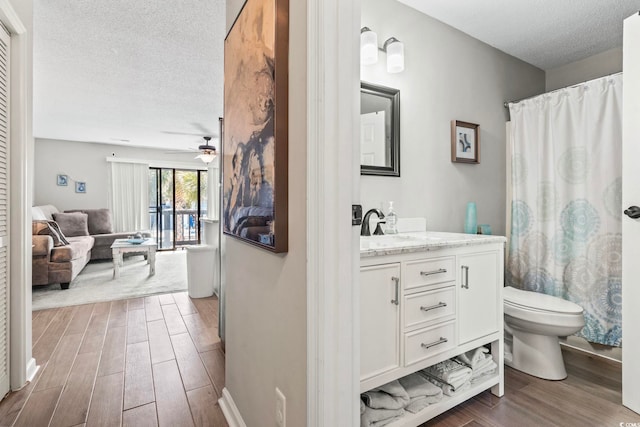 bathroom with toilet, ceiling fan, a textured ceiling, vanity, and wood finish floors