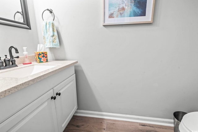 half bath featuring toilet, wood finished floors, vanity, and baseboards