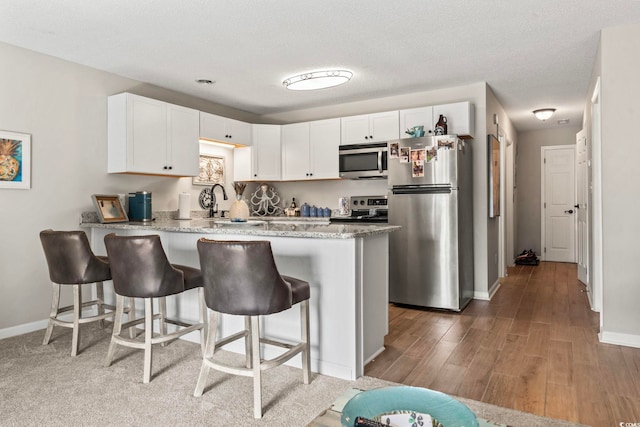 kitchen with a peninsula, appliances with stainless steel finishes, a kitchen bar, and white cabinets