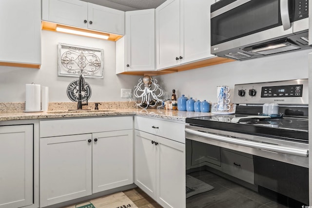 kitchen with light stone counters, a sink, wood finished floors, white cabinetry, and appliances with stainless steel finishes