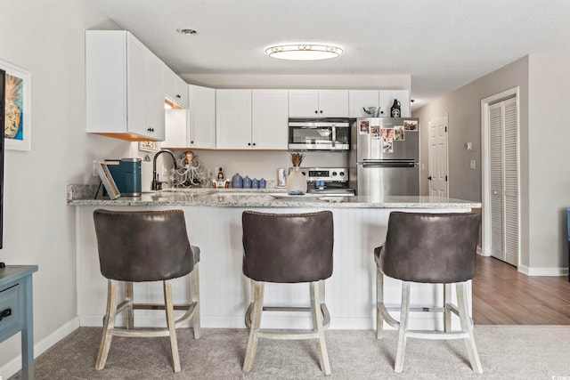 kitchen featuring appliances with stainless steel finishes, white cabinets, a sink, light stone countertops, and a peninsula