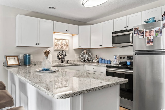 kitchen featuring a breakfast bar area, appliances with stainless steel finishes, a peninsula, white cabinetry, and a sink