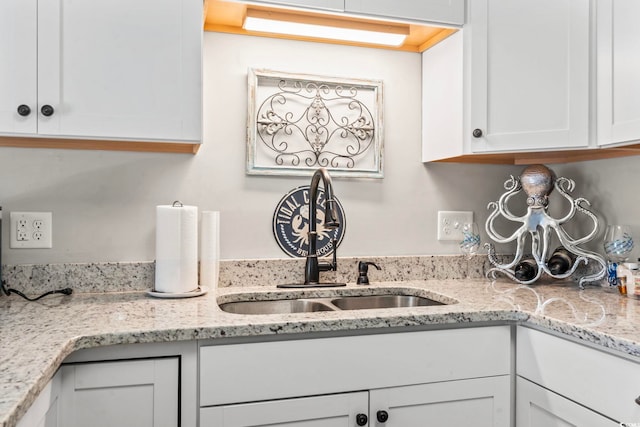 kitchen with light stone counters, a sink, and white cabinetry