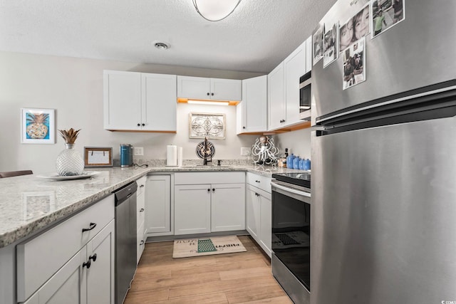 kitchen with stainless steel appliances, a sink, visible vents, white cabinetry, and light wood-type flooring