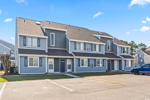 townhome / multi-family property with stucco siding, uncovered parking, a shingled roof, central AC unit, and a residential view