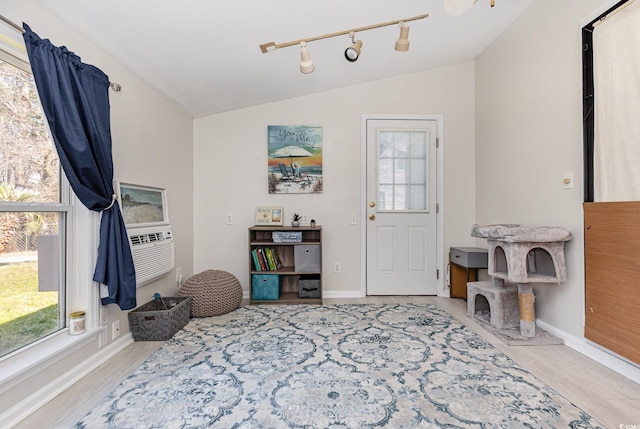 interior space featuring lofted ceiling, rail lighting, baseboards, and wood finished floors