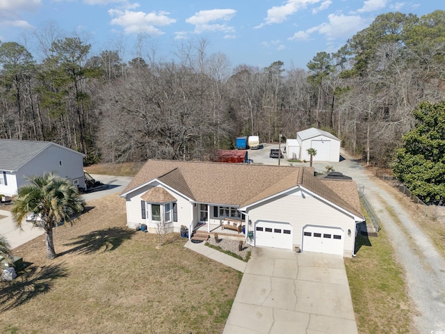 ranch-style house featuring an outbuilding, a shingled roof, a front yard, driveway, and a forest view