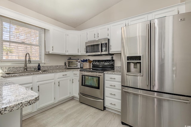 kitchen featuring light wood finished floors, vaulted ceiling, stainless steel appliances, white cabinetry, and a sink