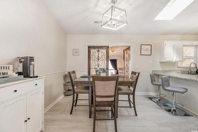 dining space featuring a skylight, visible vents, baseboards, light wood-style flooring, and a chandelier