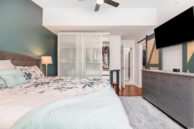 bedroom with a barn door, baseboards, wood finished floors, a walk in closet, and a closet