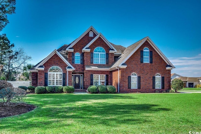 view of front of home featuring brick siding, a front yard, and a shingled roof