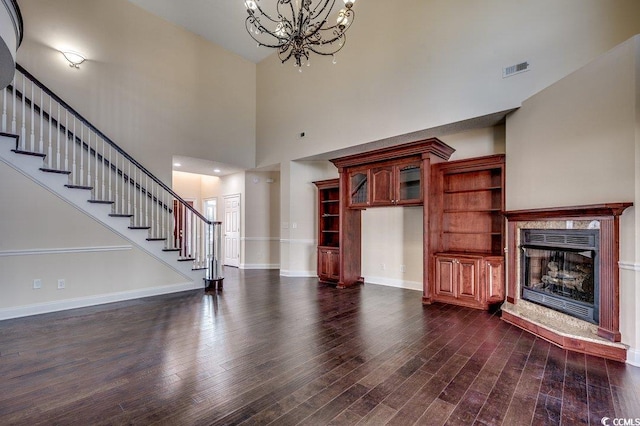 unfurnished living room with a chandelier, a high end fireplace, visible vents, dark wood-style floors, and stairway
