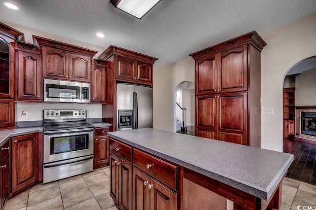 kitchen with a kitchen island, recessed lighting, a fireplace with raised hearth, arched walkways, and appliances with stainless steel finishes