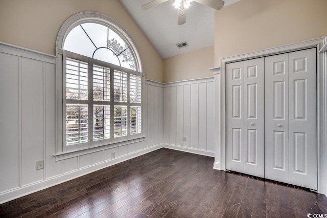 unfurnished bedroom with wainscoting, a decorative wall, wood finished floors, vaulted ceiling, and visible vents