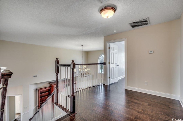 corridor featuring visible vents, a textured ceiling, wood finished floors, and an upstairs landing