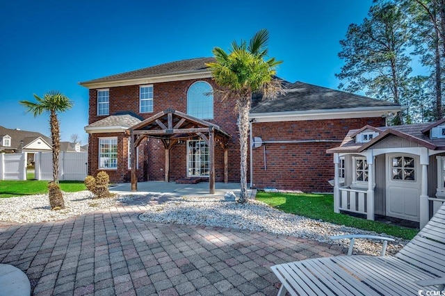 back of property with brick siding, a shingled roof, a patio area, and fence