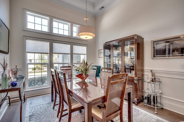 dining room with visible vents, a wainscoted wall, ornamental molding, wood finished floors, and a high ceiling