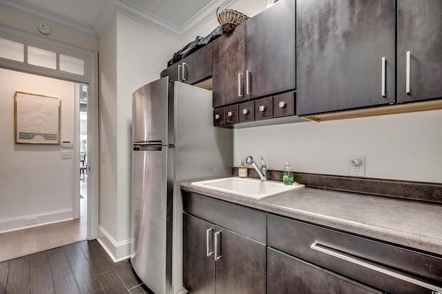 kitchen with wood finish floors, crown molding, freestanding refrigerator, a sink, and dark brown cabinets