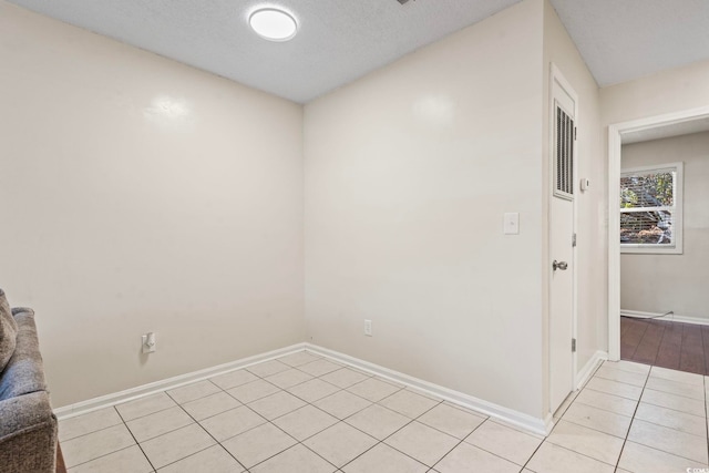 empty room with light tile patterned floors, baseboards, and a textured ceiling