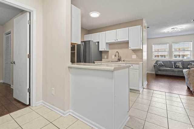 kitchen with light countertops, freestanding refrigerator, white cabinets, a sink, and light tile patterned flooring