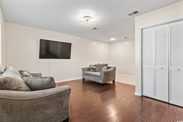 living room featuring dark wood-style floors, a textured ceiling, visible vents, and baseboards