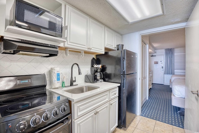 kitchen featuring light tile patterned floors, freestanding refrigerator, white cabinetry, a sink, and range with electric cooktop