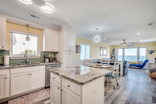 kitchen with stainless steel dishwasher, a sink, light stone counters, and pendant lighting