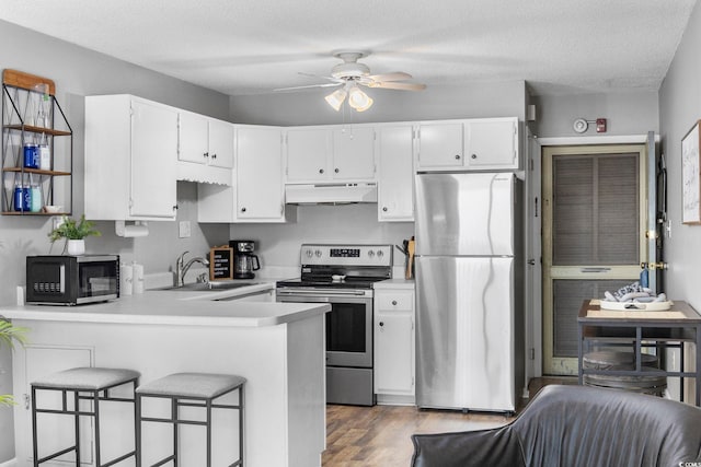 kitchen with appliances with stainless steel finishes, a peninsula, light countertops, under cabinet range hood, and a sink