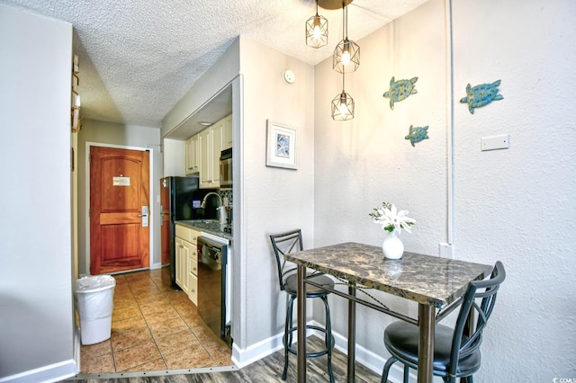 kitchen featuring a textured ceiling, cream cabinets, baseboards, black dishwasher, and freestanding refrigerator