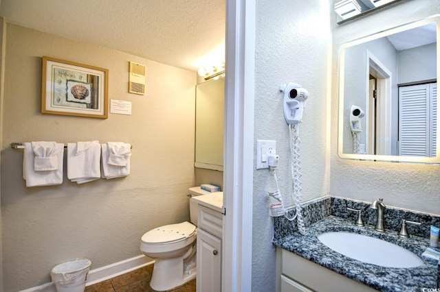 bathroom with a textured ceiling, a textured wall, tile patterned flooring, toilet, and vanity