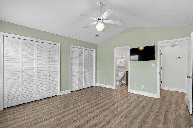 unfurnished bedroom with vaulted ceiling, wood finished floors, visible vents, and two closets