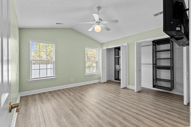 unfurnished bedroom with visible vents, two closets, baseboards, lofted ceiling, and wood finished floors