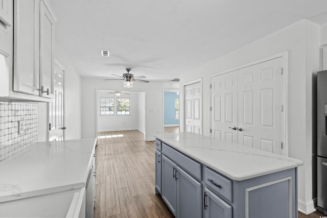 kitchen featuring visible vents, a kitchen island, wood finished floors, baseboards, and ceiling fan