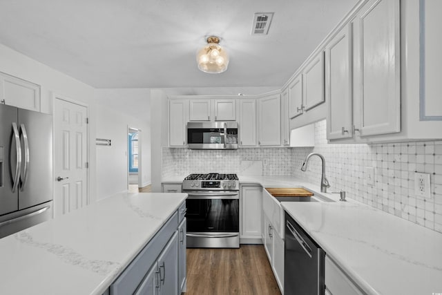 kitchen with visible vents, dark wood-type flooring, decorative backsplash, appliances with stainless steel finishes, and a sink