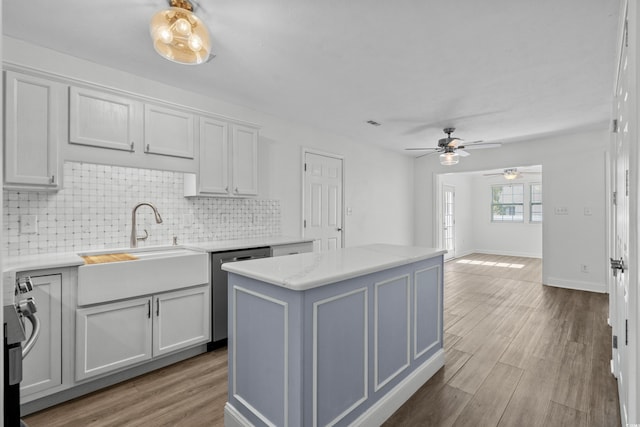 kitchen featuring wood finished floors, a sink, decorative backsplash, stainless steel dishwasher, and a center island