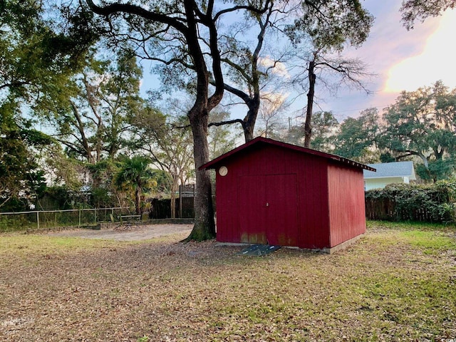 outdoor structure at dusk featuring an outbuilding, a lawn, a storage shed, and fence private yard