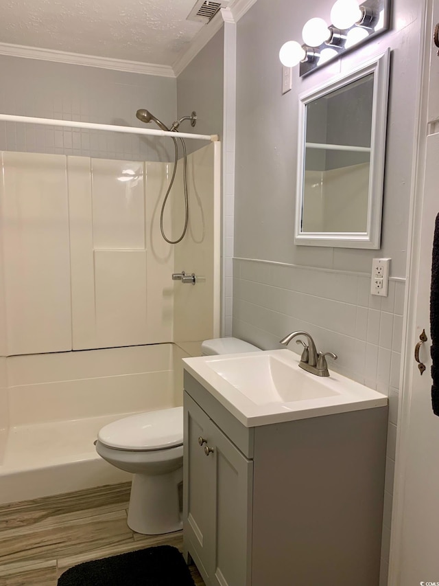 full bathroom with a shower, vanity, a textured ceiling, crown molding, and tile walls