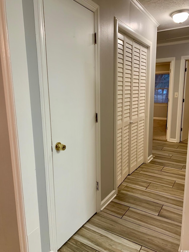 hallway featuring light wood-type flooring, crown molding, baseboards, and a textured ceiling