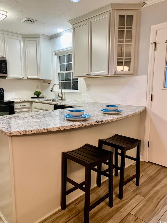 kitchen featuring a breakfast bar area, visible vents, black range with electric stovetop, stainless steel microwave, and light wood-type flooring